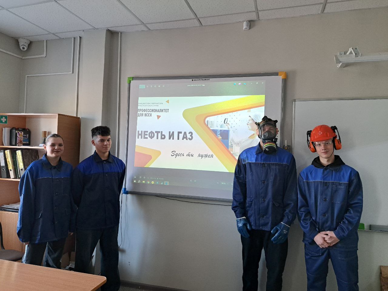 человека, стоящие перед экраном, на котором виден текст "NEФТЬ И ГАЗ". Все они одеты в синие рабочие куртки. На их головах защитные каски, а на некоторых из них также имеются респираторы. В помещении очевидно учебное или рабочее, с деревянными полками, на которых расположены книги и учебные материалы.