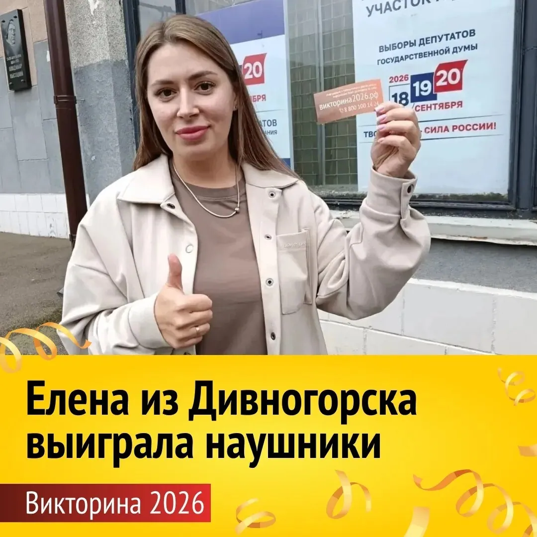 Женщина в бежевом плаще показывает большой палец вверх и держит карточку участника викторины. На фоне информационный стенд с надписью «Выборы депутатов Государственной думы 2026». Внизу плашка: «Елена из Дивногорска выиграла наушники. Викторина 2026».