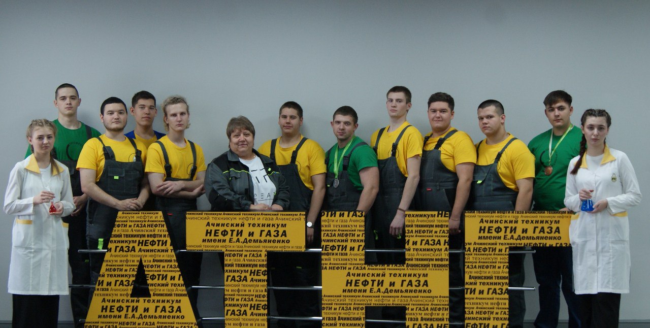 На первом изображении группа из 13 человек стоит на фоне большого знака с надписью "Нефть и газ". Все участники одеты в желтые футболки и серые комбинезоны. В центре стоит женщина с короткой стрижкой и улыбающимся лицом, вокруг нее — молодые люди разного возраста. Каждый из них выглядит уверенно, позируя для фото на нейтральном фоне, который подчеркивает яркие цвета их одежды.