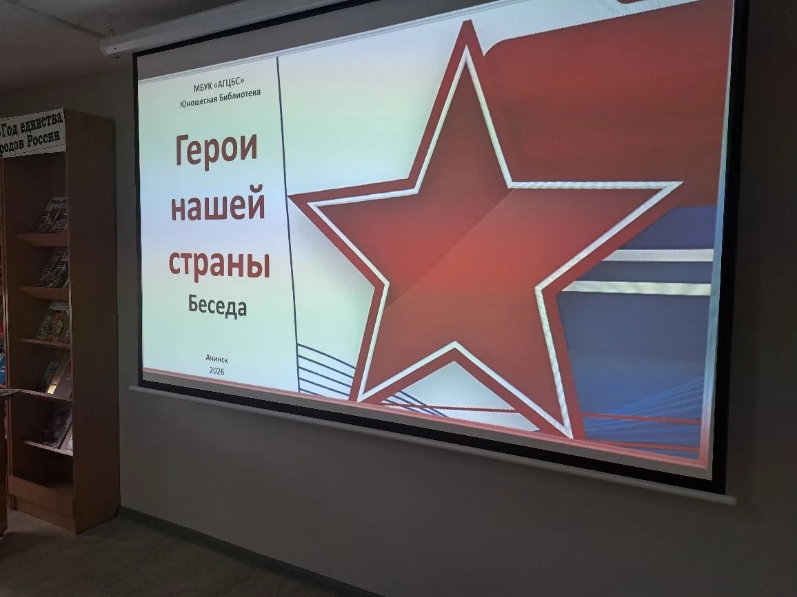 представлено плакаты с надписью "Герои нашей страны", выбранной в большом красном шрифте. Плакат оформлен с использованием цветной графики, с большой красной звездой, представляющей честь и отвагу. Фон плаката разделен на несколько цветных полос, скорее всего, символизирующих флаг России. Плакат установлен в помещении, где, возможно, происходит мероприятие, посвященное памяти героев.