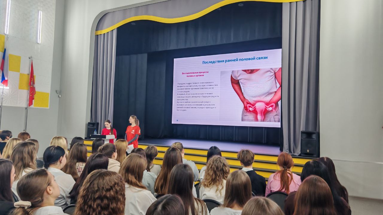 ΠΈΠ·ΠΎΠ±ΡΠ°ΠΆΠ΅Π½Ρ Π΄Π²Π΅ Π΄Π΅Π²ΡΡΠΊΠΈ Π½Π° ΡΡΠ΅Π½Π΅, ΡΠΎΠΆΠ΅ Π² ΠΊΡΠ°ΡΠ½ΡΡ
ΡΡΡΠ±ΠΎΠ»ΠΊΠ°Ρ
. ΠΠ½ΠΈ Π²ΡΡΡΡΠΏΠ°ΡΡ ΠΏΠ΅ΡΠ΅Π΄ ΡΠ»ΡΡΠ°ΡΠ΅Π»ΡΠΌΠΈ, Π° Π·Π° Π½ΠΈΠΌΠΈ Π½Π° ΡΠΊΡΠ°Π½Π΅ ΠΏΠΎΠΊΠ°Π·Π°Π½ΠΎ Π°Π½Π°ΡΠΎΠΌΠΈΡΠ΅ΡΠΊΠΎΠ΅ ΠΈΠ·ΠΎΠ±ΡΠ°ΠΆΠ΅Π½ΠΈΠ΅, ΡΠ²ΡΠ·Π°Π½Π½ΠΎΠ΅ Ρ ΡΠ΅ΠΏΡΠΎΠ΄ΡΠΊΡΠΈΠ²Π½ΡΠΌ Π·Π΄ΠΎΡΠΎΠ²ΡΠ΅ΠΌ. ΠΠ° ΡΠΊΡΠ°Π½Π΅ ΡΠ°ΠΊΠΆΠ΅ ΠΏΡΠΈΡΡΡΡΡΠ²ΡΡΡ ΠΏΠΎΡΡΠ½ΡΡΡΠΈΠ΅ ΡΠ΅ΠΊΡΡΡ ΠΈ ΡΡ
Π΅ΠΌΡ, ΠΊΠ°ΡΠ°ΡΡΠΈΠ΅ΡΡ Π·Π΄ΠΎΡΠΎΠ²ΡΡ ΠΈ ΠΌΠ΅Π΄ΠΈΡΠΈΠ½ΡΠΊΠΈΡ
ΠΏΡΠΎΡΠ΅Π΄ΡΡ. ΠΡΠ±Π»ΠΈΠΊΠ° Π² ΠΎΡΠ½ΠΎΠ²Π½ΠΎΠΌ ΡΠΎΡΡΠΎΠΈΡ ΠΈΠ· ΠΆΠ΅Π½ΡΠΈΠ½, Π²Π½ΠΈΠΌΠ°ΡΠ΅Π»ΡΠ½ΠΎ ΡΠ»ΡΡΠ°ΡΡΠΈΡ
ΠΏΡΠ΅Π·Π΅Π½ΡΠ°ΡΠΈΡ.