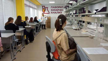 школьники сидят за рабочими местами и слушают экскурсия в лаборатории химического анализа